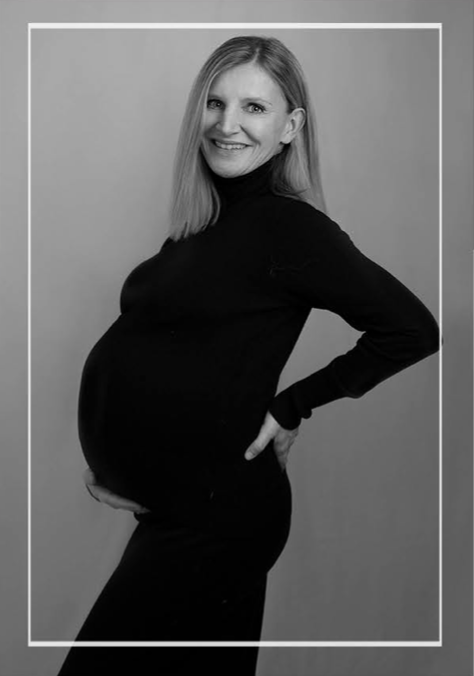 Bild zeigt eine Mutter in schwarz weiß, die selbstbewusst ihren Babybauch zeigt